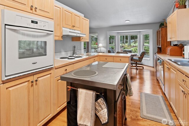 kitchen featuring white appliances, light wood-type flooring, under cabinet range hood, and light brown cabinetry