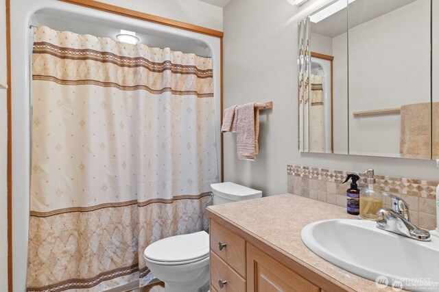 bathroom featuring curtained shower, tasteful backsplash, vanity, and toilet