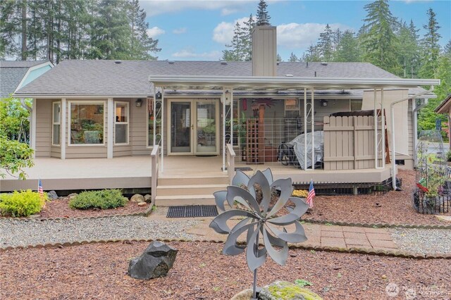 rear view of house featuring a deck, french doors, roof with shingles, and a chimney