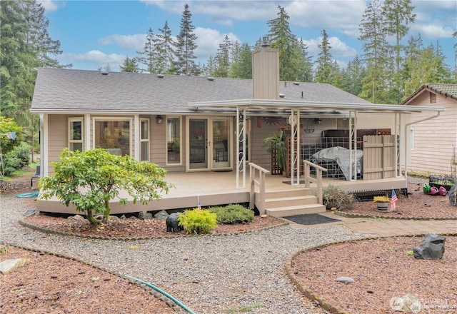 rear view of house featuring a deck, a chimney, and a shingled roof