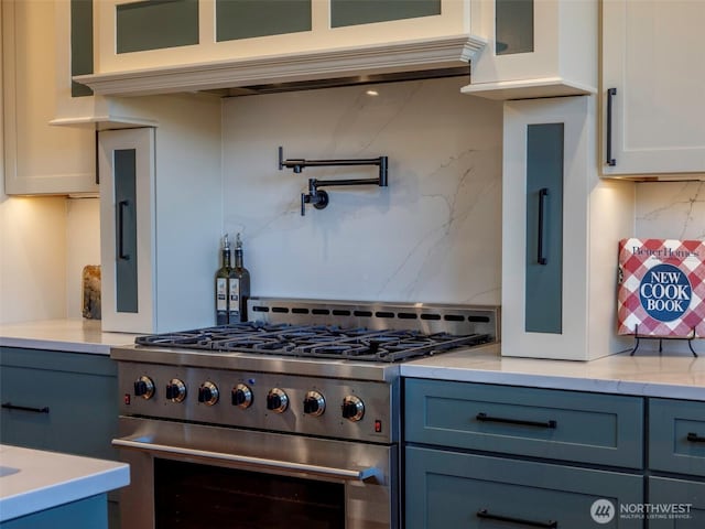 kitchen with blue cabinets, glass insert cabinets, white cabinetry, decorative backsplash, and high end range