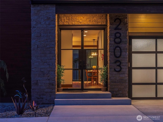 view of exterior entry featuring french doors, a garage, and stone siding