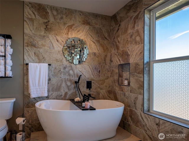 bathroom featuring tile walls, toilet, and a freestanding bath