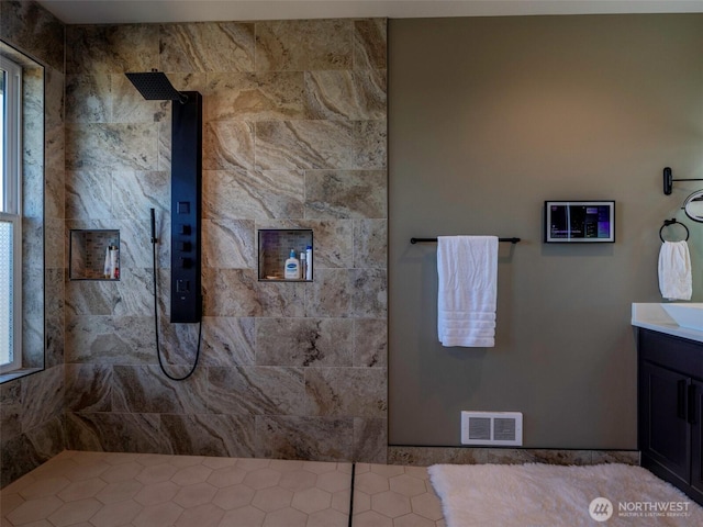 bathroom with visible vents, vanity, and a tile shower