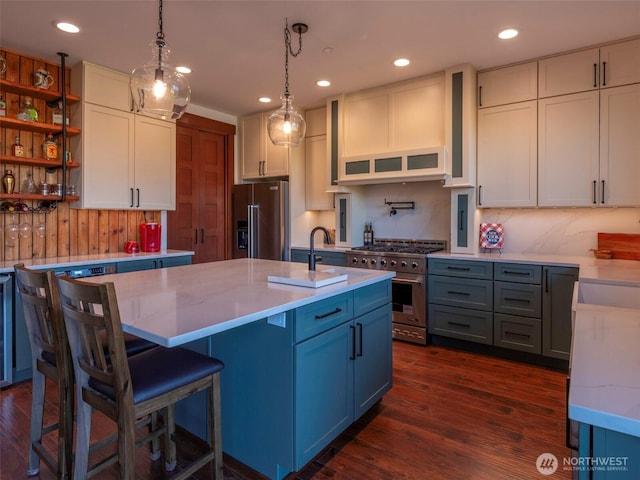 kitchen featuring a kitchen island with sink, premium appliances, dark wood finished floors, and hanging light fixtures