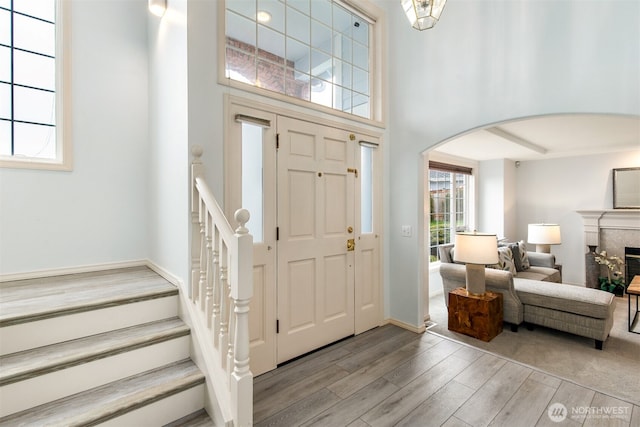 foyer featuring arched walkways, a fireplace, light wood finished floors, baseboards, and a towering ceiling