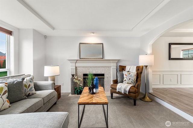 living area with arched walkways, wainscoting, carpet, and a premium fireplace