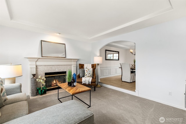 living area with a wainscoted wall, a tray ceiling, arched walkways, carpet flooring, and a premium fireplace