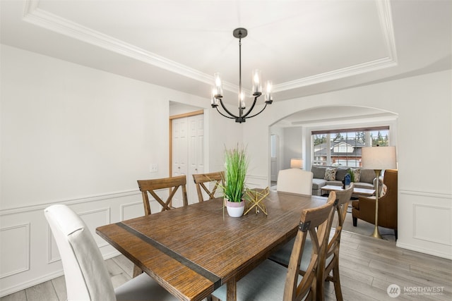 dining area featuring a tray ceiling, arched walkways, a notable chandelier, and light wood-style flooring