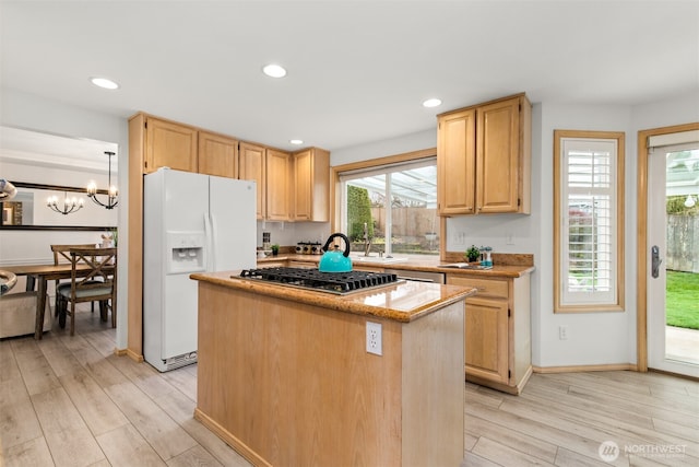 kitchen with light wood finished floors, a kitchen island, white fridge with ice dispenser, an inviting chandelier, and stainless steel gas stovetop