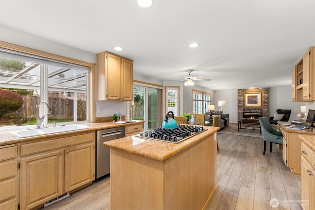 kitchen featuring light brown cabinets, a sink, stainless steel appliances, a brick fireplace, and a center island