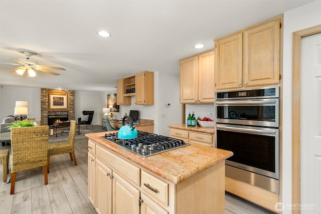 kitchen with a ceiling fan, light wood-style flooring, light brown cabinetry, appliances with stainless steel finishes, and a center island