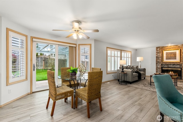 dining room with a brick fireplace, a ceiling fan, baseboards, and light wood finished floors