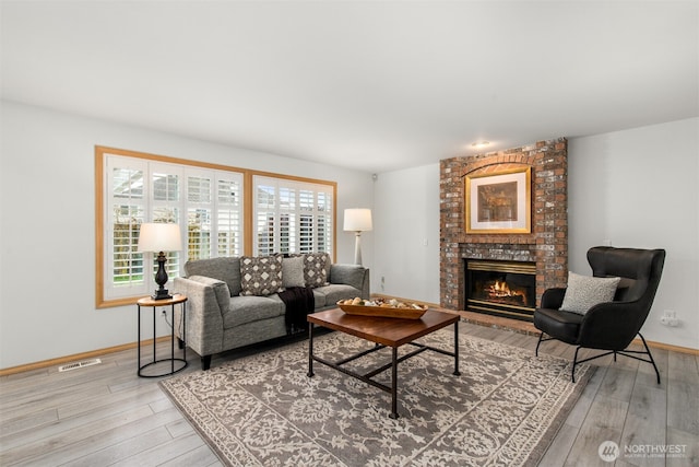 living area with visible vents, baseboards, a fireplace, and light wood finished floors