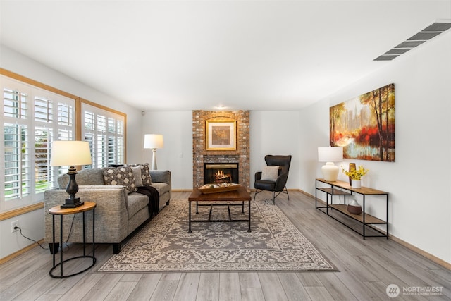 living area with a fireplace, wood finished floors, visible vents, and baseboards