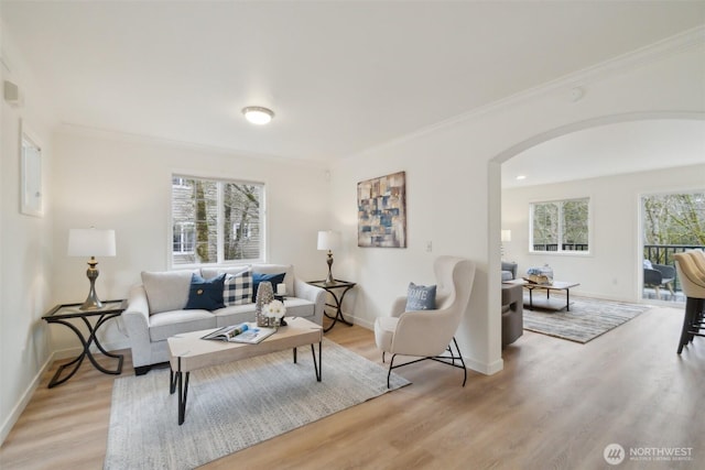 living area with baseboards, arched walkways, light wood-style flooring, and crown molding