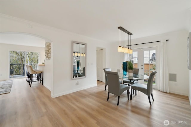 dining area with french doors, baseboards, arched walkways, and light wood finished floors