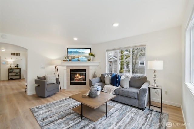 living area with baseboards, a tiled fireplace, recessed lighting, light wood-style floors, and arched walkways