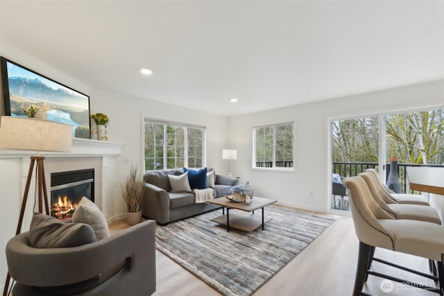 living area with a glass covered fireplace, recessed lighting, wood finished floors, and baseboards