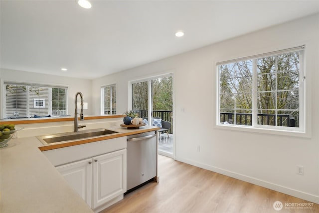 kitchen featuring light wood finished floors, dishwasher, a wealth of natural light, white cabinetry, and a sink