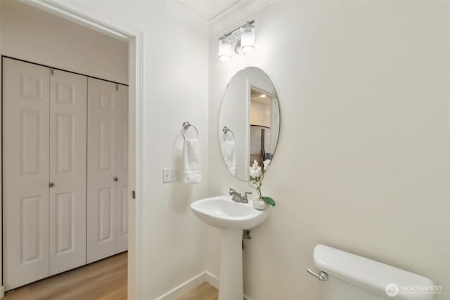 half bathroom featuring wood finished floors, baseboards, a closet, crown molding, and toilet