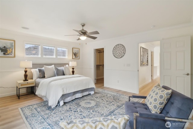 bedroom featuring light wood-type flooring, baseboards, a walk in closet, and crown molding