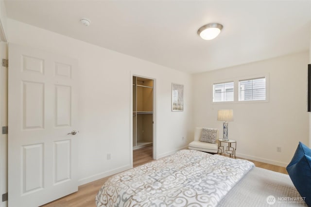 bedroom featuring a walk in closet, baseboards, and light wood-style flooring