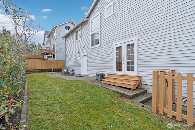 rear view of house with a lawn, entry steps, a patio, fence, and french doors