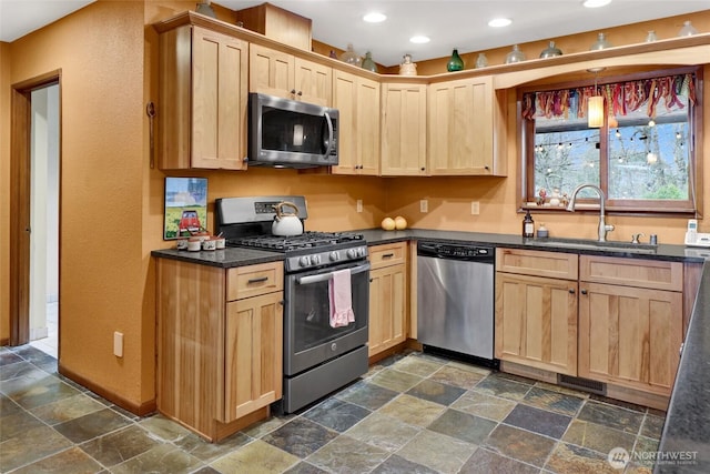 kitchen with a sink, stone finish flooring, appliances with stainless steel finishes, and light brown cabinetry