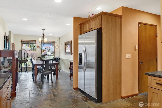 kitchen with a notable chandelier, dark countertops, stone tile flooring, recessed lighting, and stainless steel fridge