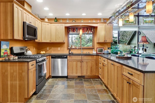 kitchen with a sink, a peninsula, light brown cabinets, and stainless steel appliances