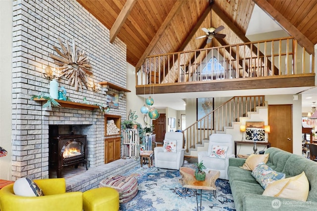 living area featuring vaulted ceiling with beams, ceiling fan, stairs, wooden ceiling, and a brick fireplace