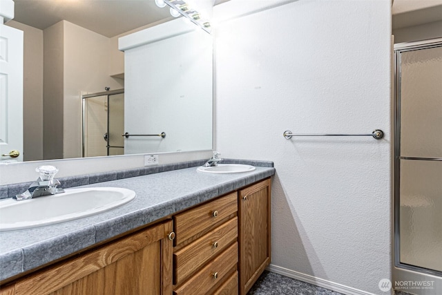 full bathroom with a shower stall, double vanity, baseboards, and a sink