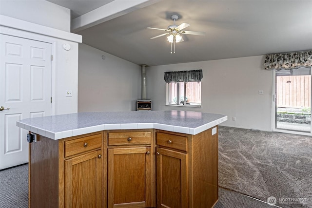 kitchen featuring carpet, lofted ceiling with beams, a wood stove, brown cabinetry, and a ceiling fan