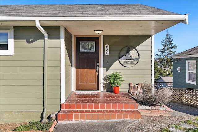 entrance to property with covered porch and roof with shingles