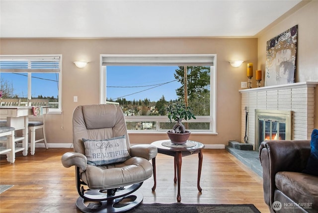 living room with light wood-style flooring, a brick fireplace, and baseboards