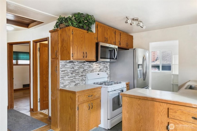 kitchen with brown cabinets, tasteful backsplash, wood finished floors, stainless steel appliances, and light countertops