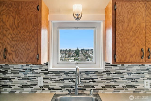 kitchen with a sink, tasteful backsplash, brown cabinetry, and light countertops