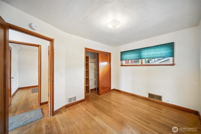 unfurnished bedroom with light wood finished floors, baseboards, visible vents, and a closet