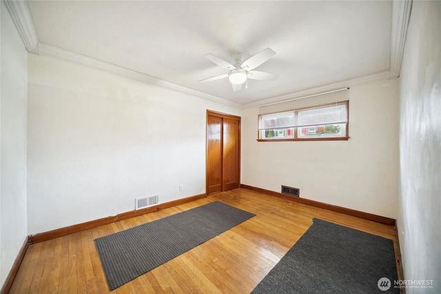 empty room featuring ornamental molding, visible vents, wood-type flooring, and ceiling fan