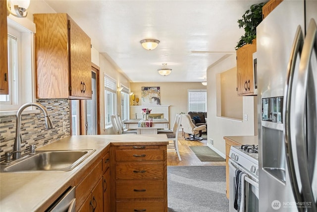 kitchen with a sink, stainless steel appliances, a peninsula, light countertops, and decorative backsplash