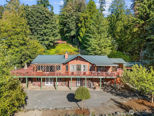 back of property with a standing seam roof, a wooden deck, a patio area, and metal roof