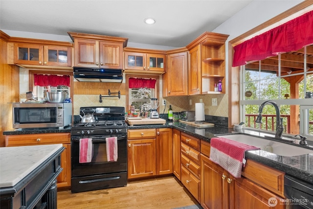 kitchen featuring black appliances, light wood-style flooring, under cabinet range hood, a sink, and brown cabinetry