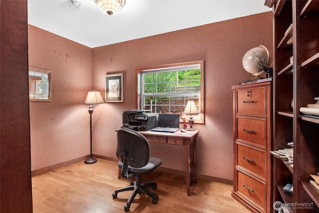 office area with light wood-style flooring, a textured wall, and baseboards