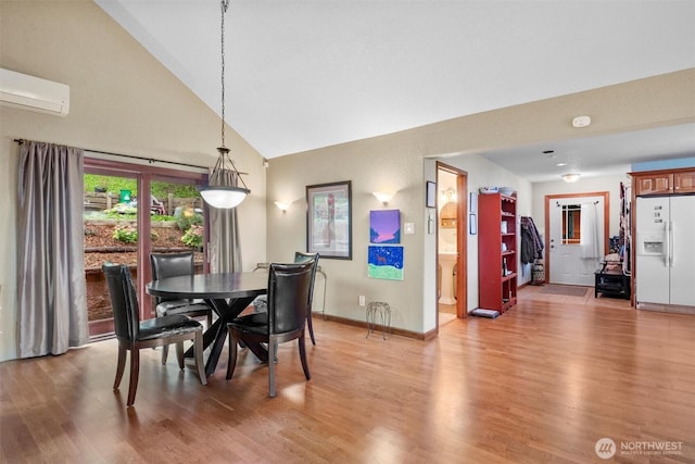 dining room with baseboards, light wood-style floors, an AC wall unit, and high vaulted ceiling