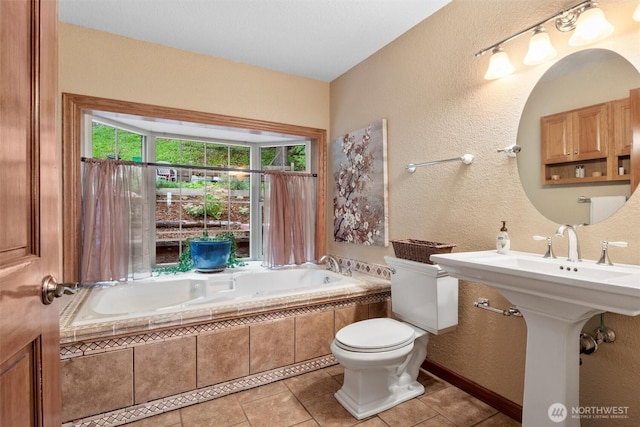 bathroom with a bath, tile patterned floors, toilet, and a textured wall