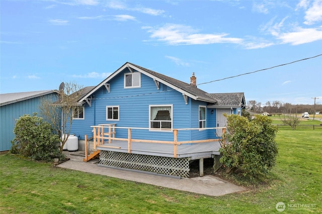 back of house featuring a lawn, a chimney, a deck, and a shingled roof