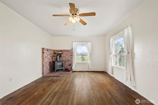 unfurnished living room featuring a ceiling fan, a wood stove, and hardwood / wood-style flooring