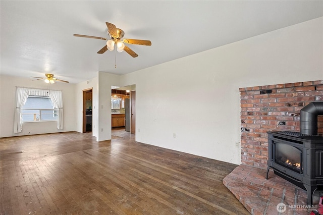 unfurnished living room with a wood stove, wood-type flooring, and ceiling fan