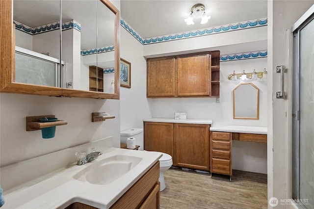 full bathroom featuring a shower with shower door, toilet, wood finished floors, and vanity